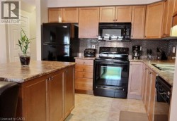 Kitchen featuring wood-finish cabinetry, a central island with a countertop, black appliances, a tile backsplash, and tile flooring - 