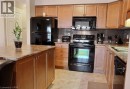 Kitchen featuring wood-finish cabinetry, a central island with a countertop, black appliances, a tile backsplash, and tile flooring - 507 Beaumont Crescent, Kitchener, ON 
