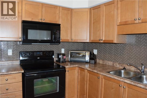 Light wood-finish cabinetry, patterned backsplash, double basin stainless steel sink, black range, and built-in microwave - 507 Beaumont Crescent, Kitchener, ON 