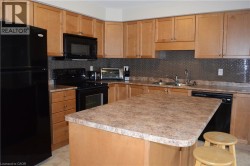 Kitchen featuring wood cabinetry, an island with countertop, black appliances, double basin sink, and a textured backsplash - 