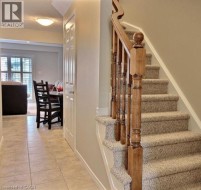 Wood-finish staircase railing with carpeted stairs, tiled flooring, and white paneled doors - 