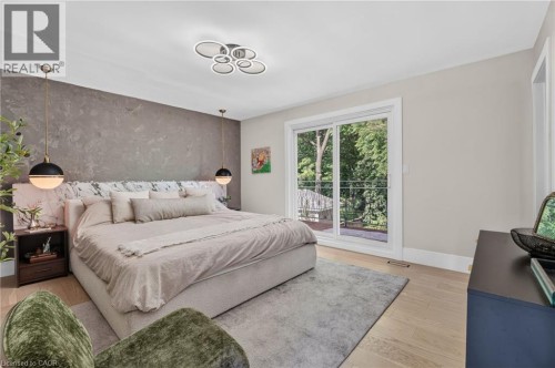 Spacious bedroom featuring light wood-finish flooring, a textured accent wall, and a contemporary ceiling light fixture - 9 Leslie Drive, Hamilton, ON 
