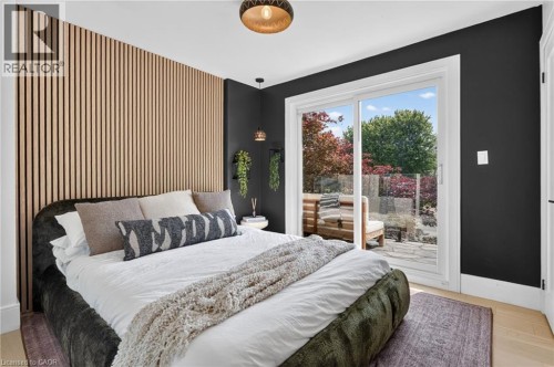 Bedroom with a slatted wood accent wall, light wood-finish flooring, and a sliding glass door leading to a stone patio - 9 Leslie Drive, Hamilton, ON 