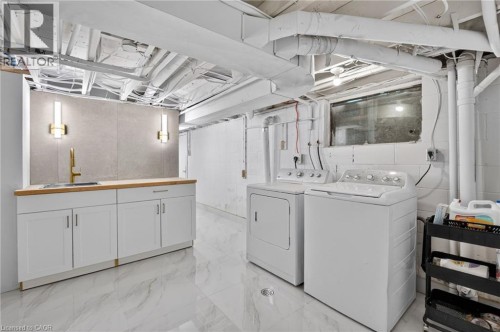 Laundry area featuring white appliances, a wood-finish countertop, a built-in sink with a gold-finish faucet, and a stone-look backsplash - 9 Leslie Drive, Hamilton, ON 