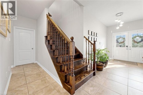 Hardwood staircase with turned spindles, tile flooring, white interior doors, and double entry doors with decorative glass inserts - 173 Raymond Road, Ancaster, ON 
