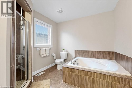 Full bathroom featuring a built-in soaking tub, a separate glass-enclosed shower with tile surround, a single window, and textured wood-finish floor tiling - 173 Raymond Road, Ancaster, ON 