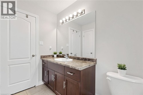 Bathroom featuring a dark wood-finish vanity with ample storage, an integrated sink, a spacious wall mirror, and a contemporary light fixture - 173 Raymond Road, Ancaster, ON 