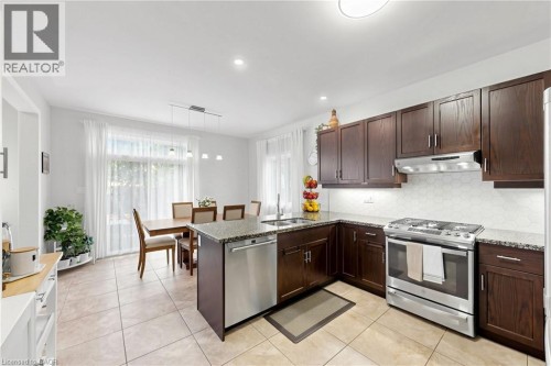 Kitchen featuring dark wood cabinetry, stainless steel appliances, speckled countertops, and a hexagonal tile backsplash - 173 Raymond Road, Ancaster, ON 