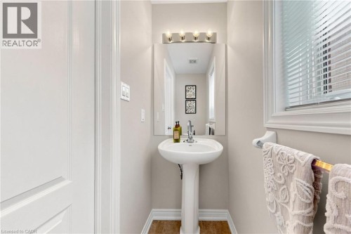 Pedestal sink with chrome faucet, wall-mounted mirror, brushed nickel vanity lighting, and wood-finish flooring - 173 Raymond Road, Ancaster, ON 