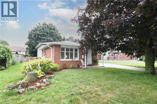 Red brick exterior with white window trim, mature front yard tree, established front yard landscaping, and a paved driveway - 219 Foxhunt Road, Waterloo, ON 