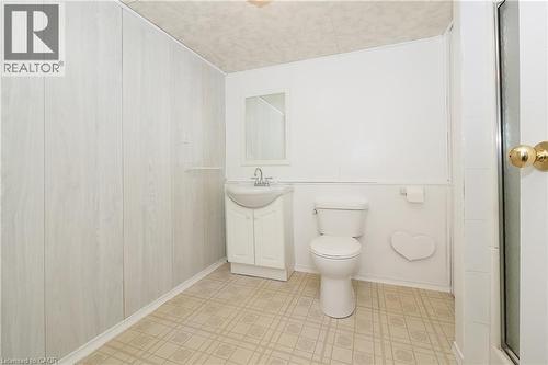 White wood-finish paneling, white vanity with integrated sink, toilet, wall-mounted mirror, and tiled flooring - 219 Foxhunt Road, Waterloo, ON 