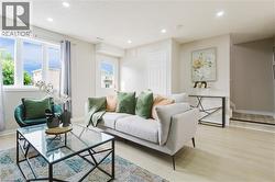 Recessed ceiling lighting, light wood-finish flooring, multiple windows, a white paneled door, and a partially visible staircase - 