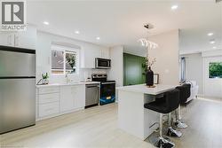White kitchen cabinetry with gold-tone hardware, stainless steel appliances, a center island with countertop seating, recessed lighting, and wood-finish flooring - 