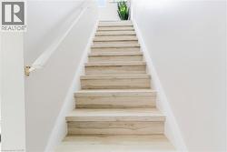 Staircase featuring light wood-finish treads and risers, white painted walls, and a white handrail with brass-tone brackets - 