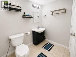 White pedestal toilet, dark wood-finish vanity with integrated sink, wall-mounted vanity mirror, three-bulb vanity light fixture, and tile flooring - 
