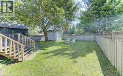 Expansive backyard featuring a wood deck with stairs, mature trees, a storage shed, and perimeter fencing - 