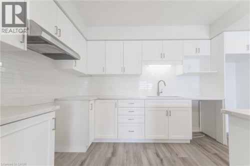 White cabinetry with brushed nickel hardware, stainless steel range hood, white subway tile backsplash, light-toned countertops, and wood-finish flooring - 25 Urbane Boulevard, Kitchener, ON 