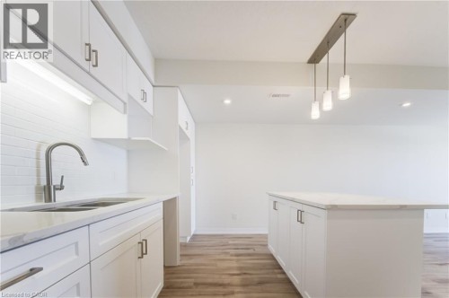 White shaker-style cabinetry with brushed nickel hardware, light-toned countertops, a stainless steel sink with a gooseneck faucet, white subway tile backsplash, and wood-finish flooring - 25 Urbane Boulevard, Kitchener, ON 