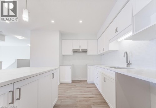 White cabinetry with modern hardware, light-toned wood-finish flooring, recessed lighting, white countertops, and a stainless steel range hood - 25 Urbane Boulevard, Kitchener, ON 