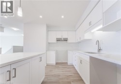 White cabinetry with modern hardware, light-toned wood-finish flooring, recessed lighting, white countertops, and a stainless steel range hood - 