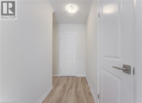 Hallway featuring wood-finish flooring, white paneled doors, and a flush mount ceiling light - 25 Urbane Boulevard, Kitchener, ON 
