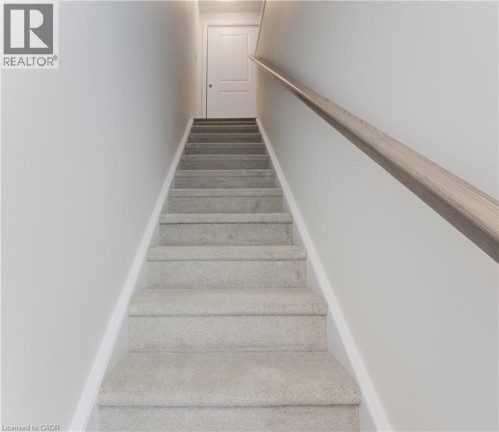 Carpeted staircase with light-toned wall finishes, a modern light wood-finish handrail, and white trim accents - 25 Urbane Boulevard, Kitchener, ON 