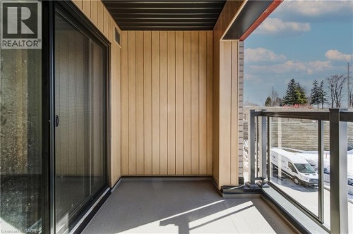 Sliding glass door access to an outdoor balcony featuring a glass and metal railing, vertical paneling, and an overhead soffit - 25 Urbane Boulevard, Kitchener, ON 