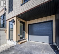 Exterior with light brick siding and wood-finish paneling, featuring a dark overhead garage door, a black framed entry door, and exterior wall sconces - 