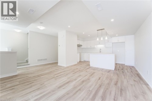 Open-concept design featuring wood-finish flooring, recessed lighting, and a kitchen with white cabinetry, a central island, and pendant lighting - 25 Urbane Boulevard, Kitchener, ON 