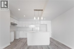 Modern kitchen featuring white cabinetry, a central island, wood-finish flooring, recessed lighting, and a linear pendant fixture - 