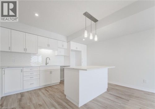 White cabinetry with brushed nickel hardware, white subway tile backsplash, white countertop, stainless steel sink with a gooseneck faucet, and wood-finish flooring - 25 Urbane Boulevard, Kitchener, ON 