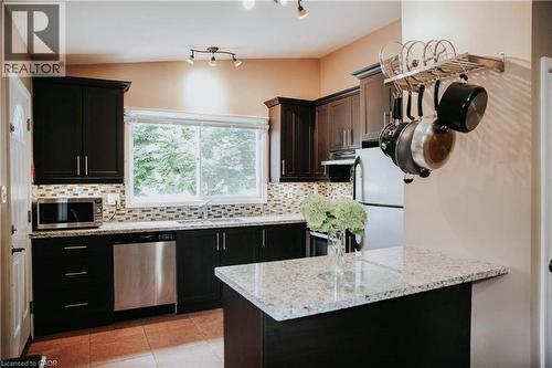 Kitchen featuring dark wood cabinetry, light-toned countertops, a mosaic tile backsplash, stainless steel appliances, and a window above the sink - 1 Vera Court, Hamilton, ON 