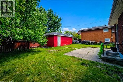 Expansive grassy yard with a concrete patio, mature trees, a red storage shed, and a wooden fence - 1 Vera Court, Hamilton, ON 