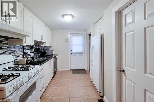 Kitchen with white cabinetry, dark countertops, a mosaic tile backsplash, a gas range, and tile flooring - 1 Vera Court, Hamilton, ON 