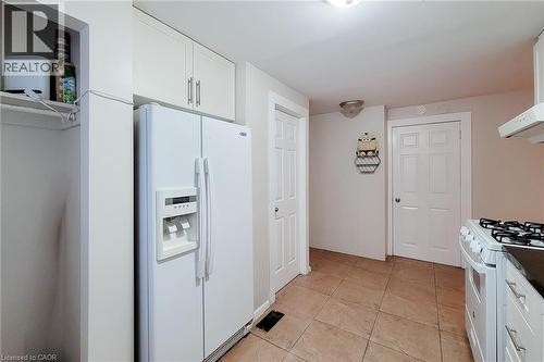 White kitchen cabinetry with brushed nickel hardware, side-by-side refrigerator, tile flooring, and white paneled doors - 1 Vera Court, Hamilton, ON 