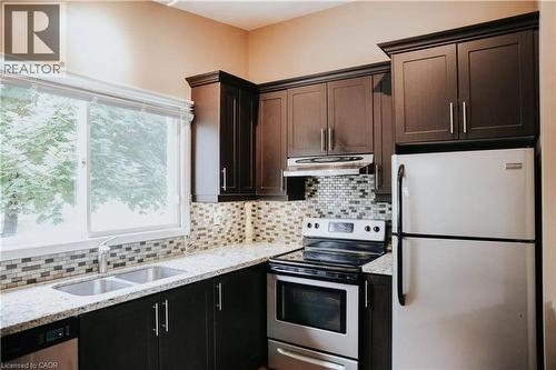 Kitchen featuring dark wood-finish cabinetry, light speckled countertops, a mosaic tile backsplash, and stainless steel appliances - 1 Vera Court, Hamilton, ON 