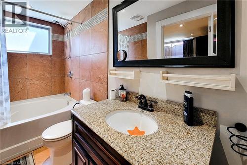 Integrated bathtub and shower with brown tile surround, a frosted glass window, a vanity with a granite-style countertop, and a dark wood-finish cabinet - 1 Vera Court, Hamilton, ON 