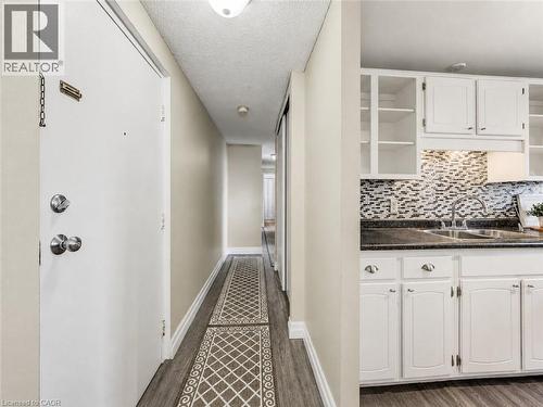 Kitchen featuring white cabinetry, dark countertops, and a mosaic tile backsplash - 4 Avalon Place Unit# 303, Kitchener, ON 