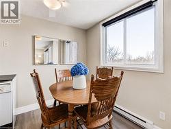 Bright dining area with large windows framing natural light, wood-finish round table, wood chairs with vertical slat backs, white ceramic vase accent, and wood-finish flooring throughout - 