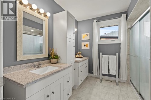 Bathroom featuring a single vanity with a rectangular sink, speckled countertop, white cabinetry, and a glass-enclosed shower - 87 Monte Drive, Hamilton, ON 