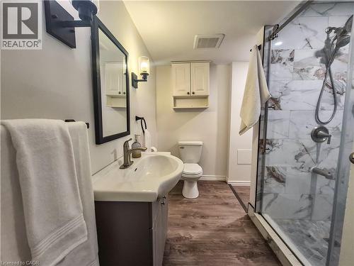 Glass-enclosed shower with tiled walls and floor, vanity with an integrated sink, wood-finish flooring, and wall-mounted lighting fixtures - 11 Duncairn Avenue, Kitchener, ON 