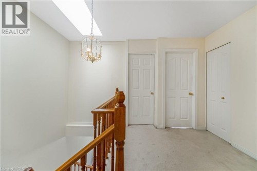 Skylight and ceiling-mounted chandelier illuminate the upper landing with white panel doors, wood banister, and carpeted flooring - 82 Milner Downs Crescent, Ottawa, ON 
