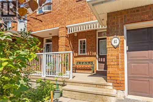 Brick exterior with a covered porch, white railing, concrete steps, and a dark wood entry door - 82 Milner Downs Crescent, Ottawa, ON 