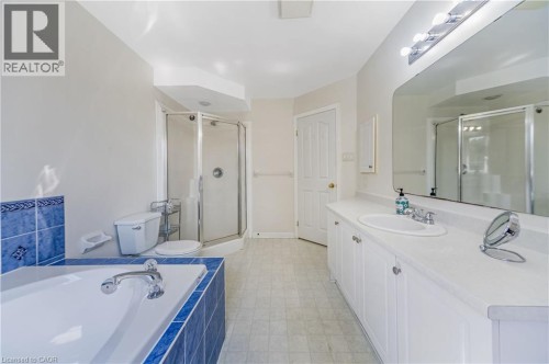 Spacious bathroom featuring a built-in bathtub with blue tile surround, glass-enclosed shower, and an extended vanity with dual sinks - 82 Milner Downs Crescent, Ottawa, ON 
