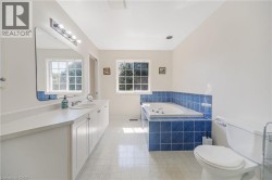 Dual window placement, built-in bathtub with blue tile surround, vanity with integrated sink, rectangular mirror with overhead lighting, and white toilet - 