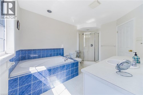 Soaking tub with blue tile surround, glass-enclosed shower, single vanity with integrated sink, and recessed lighting - 82 Milner Downs Crescent, Ottawa, ON 
