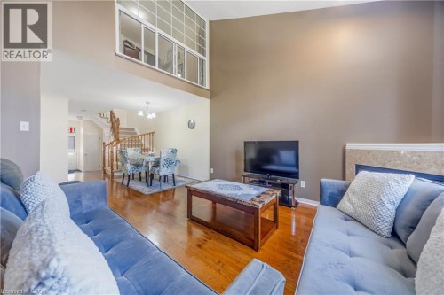 Two-story living area with high ceilings, wood-finish flooring, a fireplace with a stone surround, and an upper-level window bank - 82 Milner Downs Crescent, Ottawa, ON 