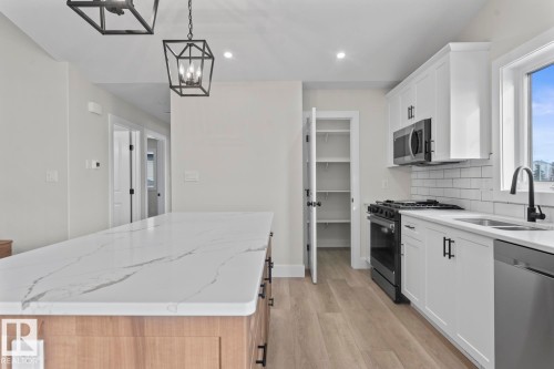 The kitchen features a spacious island with a marble-effect countertop, white cabinetry with black hardware, and a stainless steel dishwasher - 807 Schooner Drive, Cold Lake, AB - Indoor Photo Showing Kitchen With Double Sink With Upgraded Kitchen