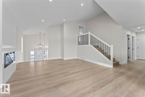 The property features light-toned flooring, a fireplace with a visible firebox, and a staircase with light-toned treads and dark-toned spindles - 807 Schooner Drive, Cold Lake, AB - Indoor Photo Showing Other Room