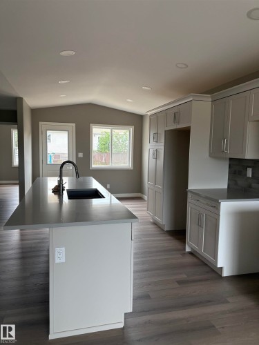 Kitchen featuring dark wood-style floors, an island with sink, lofted ceiling, light stone countertops, and backsplash - 7413 44 Avenue, Camrose, AB - Indoor Photo Showing Kitchen With Double Sink